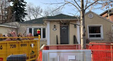 A house under renovation with workers installing flooring and working on walls, showcasing an active home remodeling project.